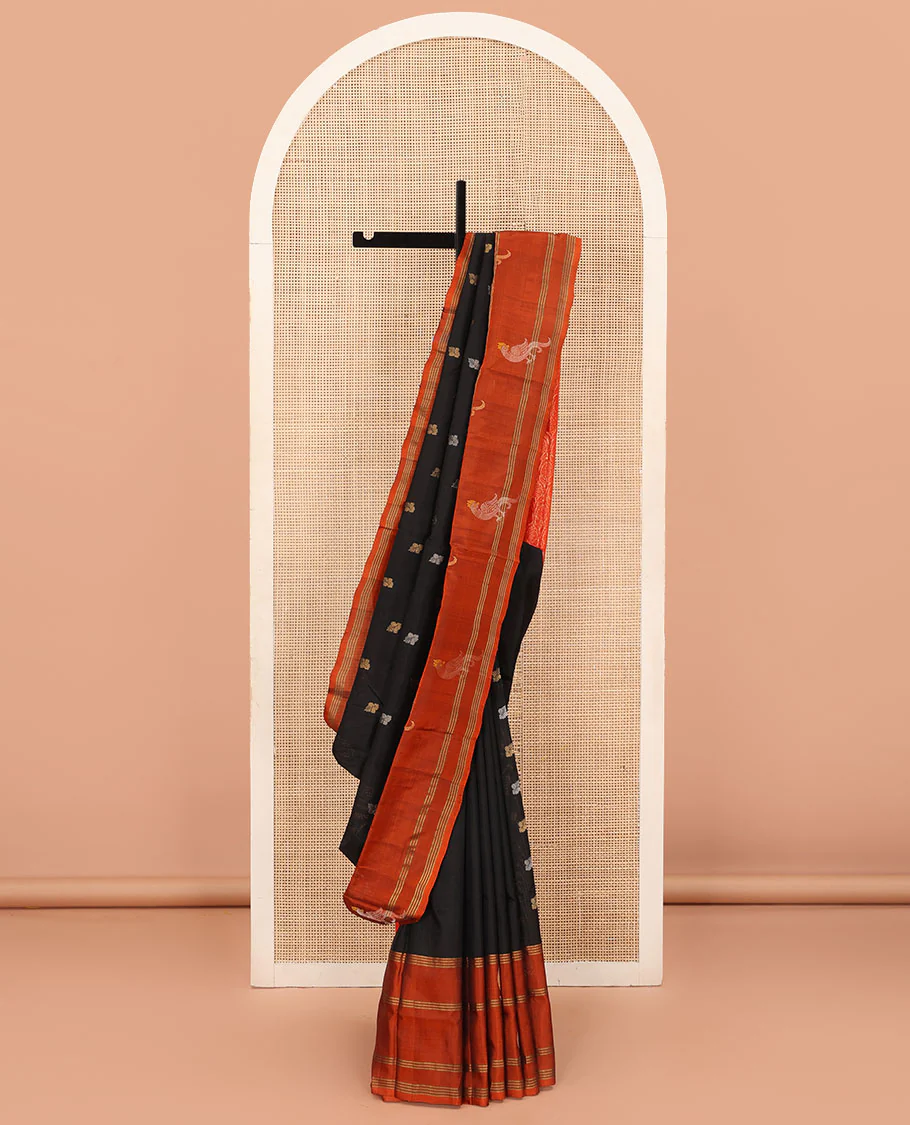 Inky Black Uppada Silk Saree Enlivened With Zari Buttas, Captivating Contrast Border Featuring Zari Stripes And Peacock Motifs, Pallu Depicting Rose Flower-Enclosed Mughal-Style Arches, And Paired With A Contrast Blouse