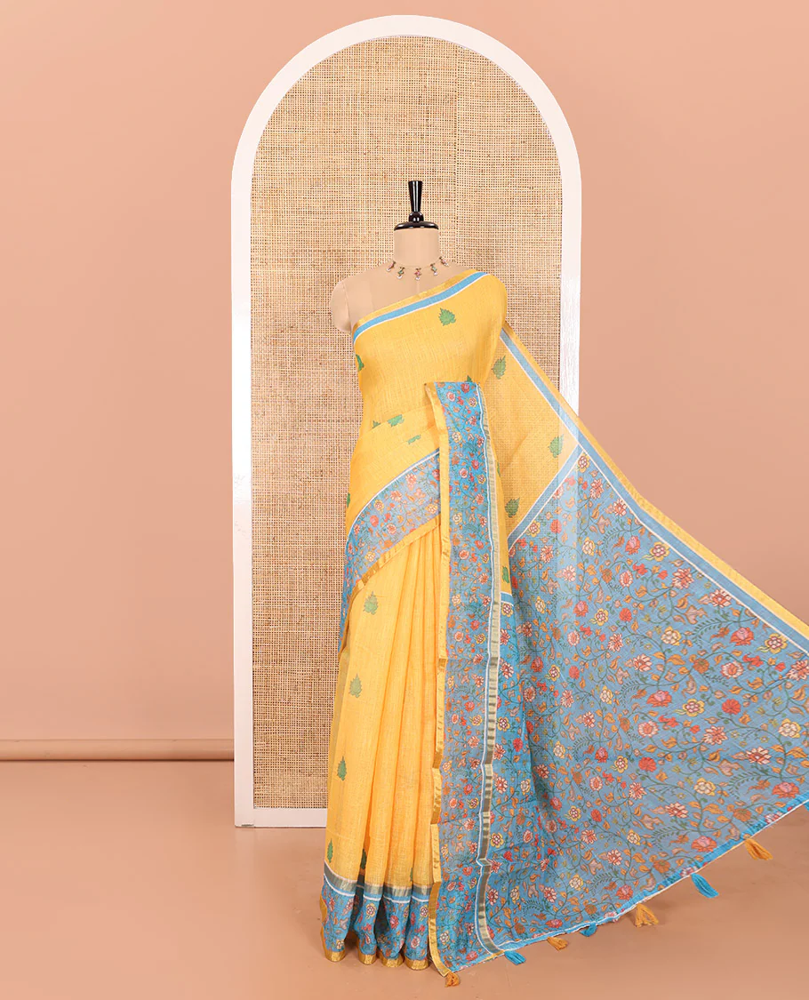 Yellow Linen Saree Detailed with Leaf Motifs All Over Its Body, Complemented by a Contrast Floral Vine Printed Border, Pallu Mirrors the Floral Vine Print, and Paired with a Contrast Floral Printed Blouse